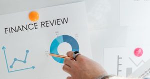 Mão apontando para um gráfico financeiro na parede, ilustrando a análise de dados e revisão.